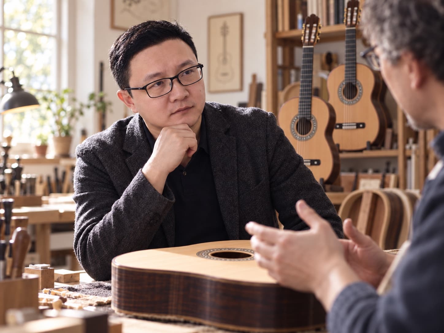 焦旭辉在吉他工作室与制作者交流，背景展示卓拉 C5 风格的古典吉他主题图